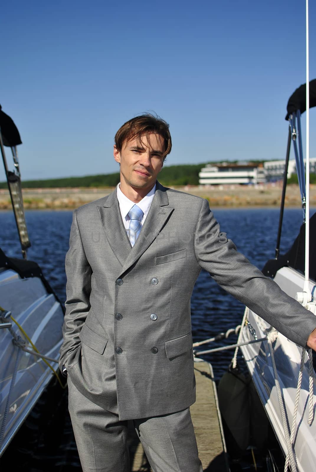 man in a gray suit, standing on the beach near the yacht