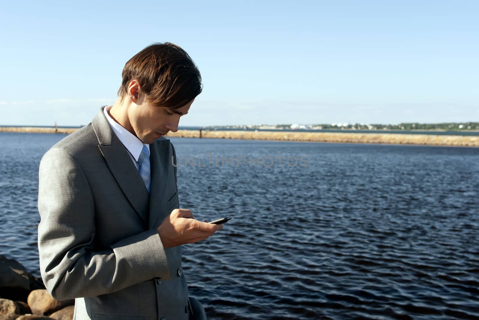 man in a gray suit dials the phone against the sea