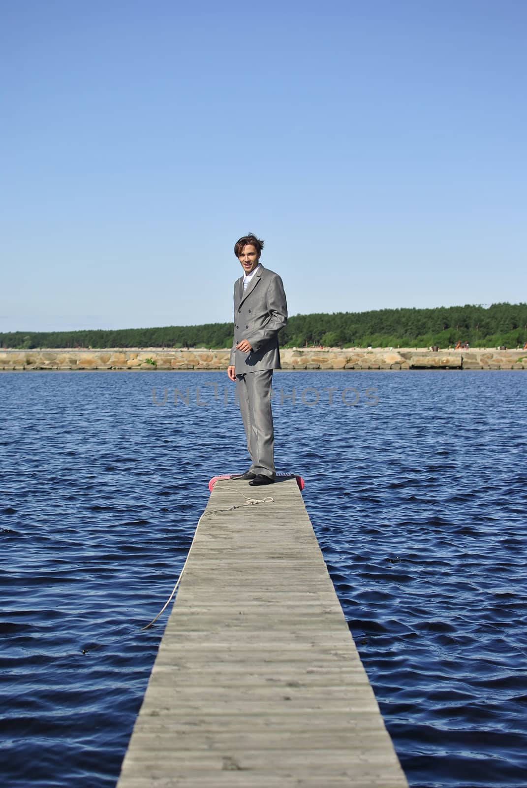 man in a gray business suit standing on a pier near the sea