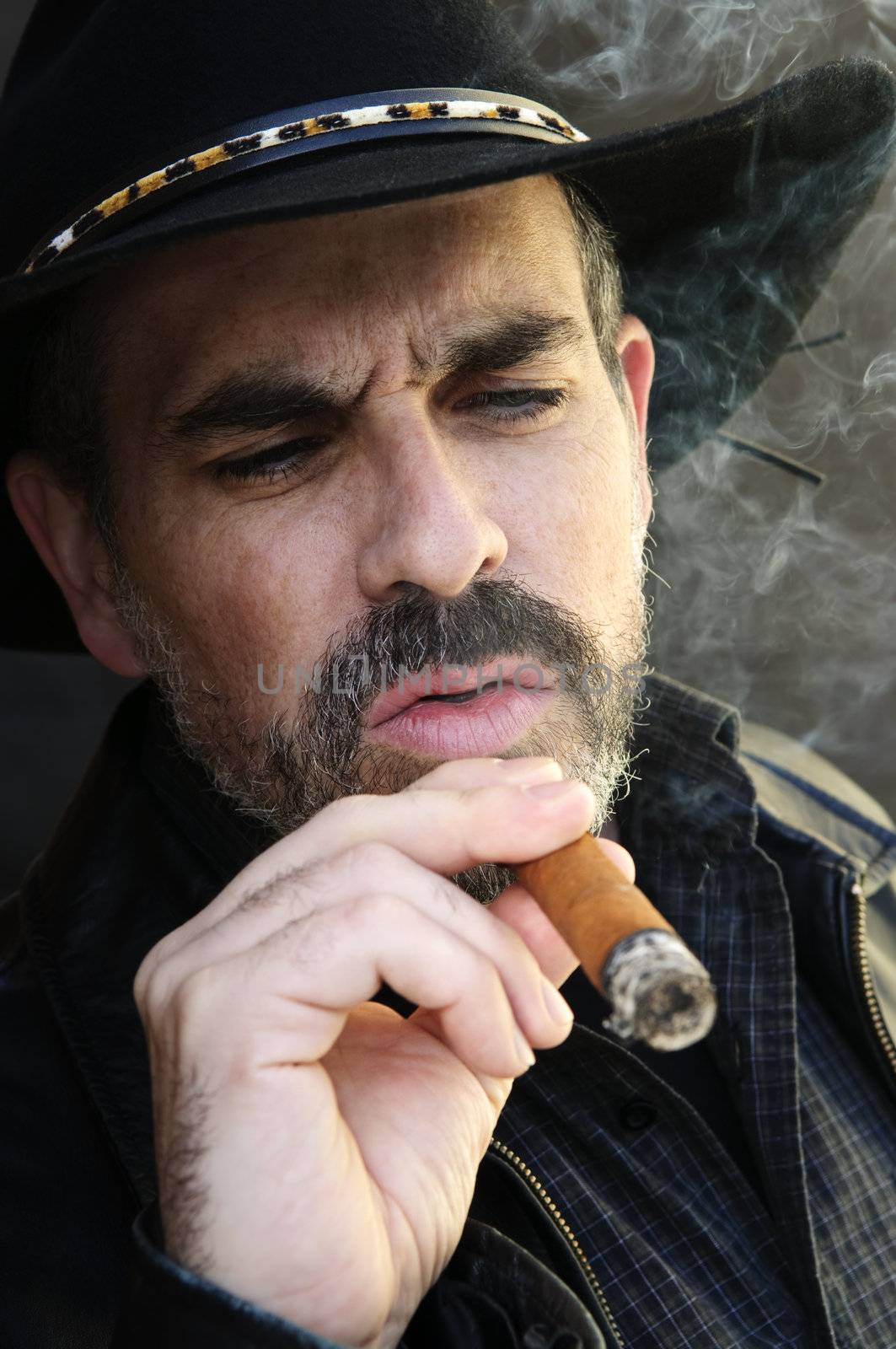 Man with beard in cowboy hat smoking cigar