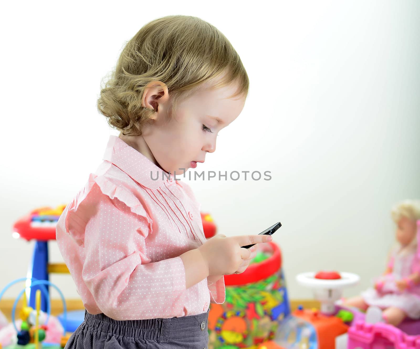 little girl standing with mobile phone in room with toys