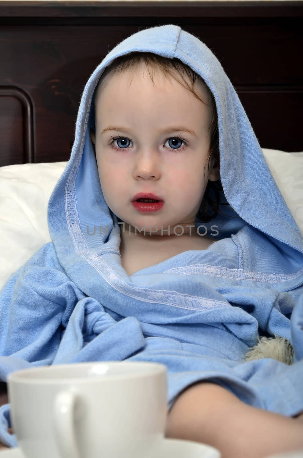 little girl in a blue robe resting on the bed after a shower with a cup of tea