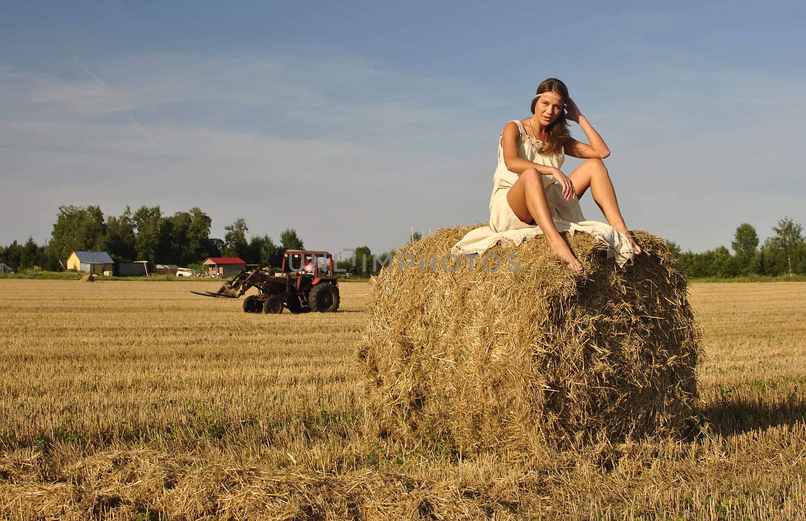 girl in a rural clothing sitting on the haystack, tractor on the background. space for text