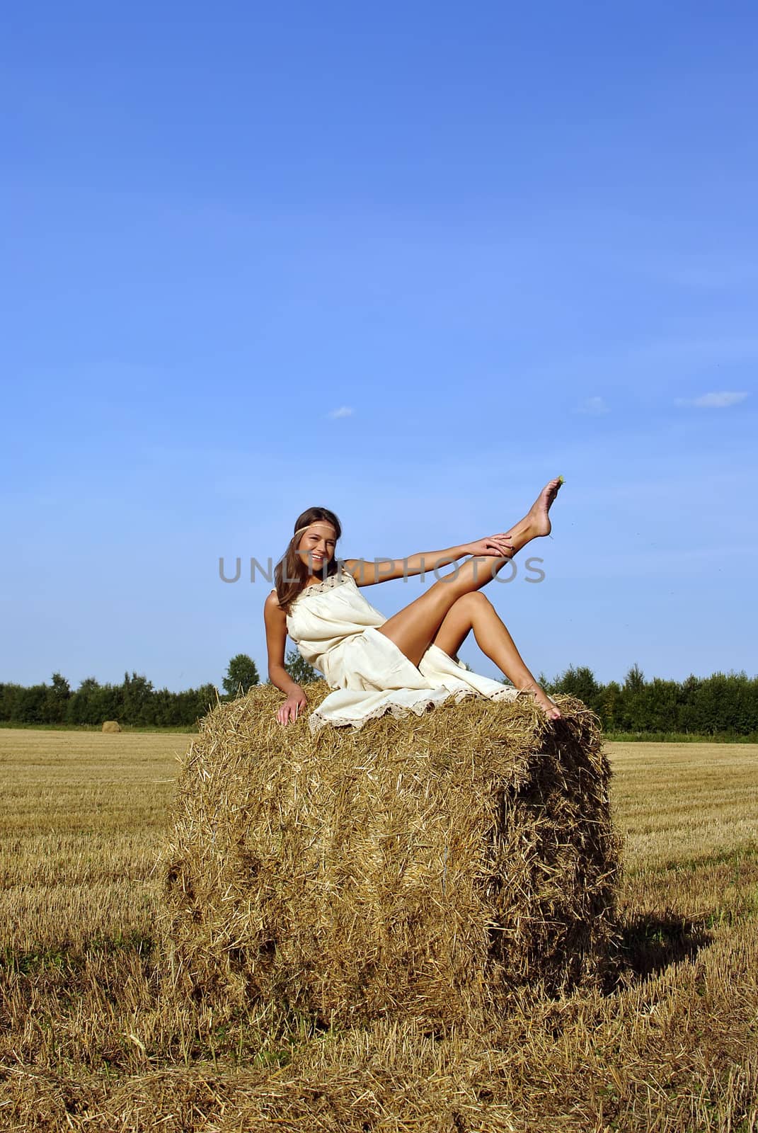 smiling girl in a rural clothing sitting on the haystack with leg up. space for text