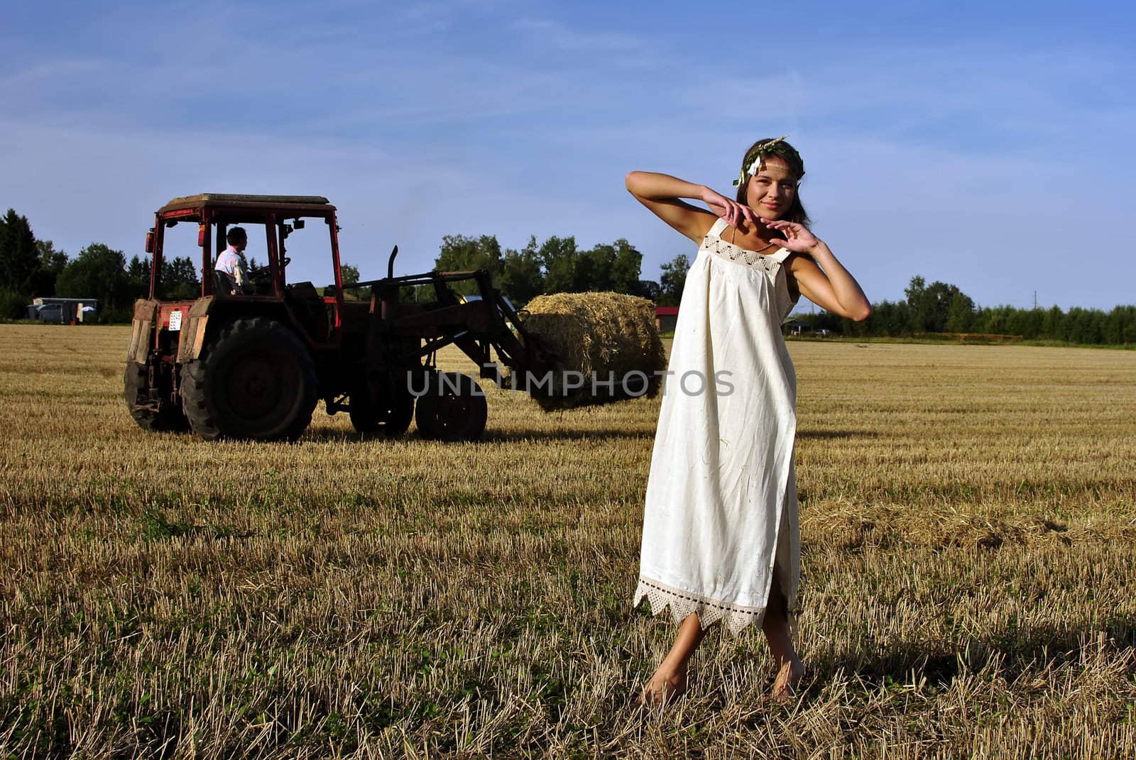 girl in a rural clothing standing on the field, tractor on the background