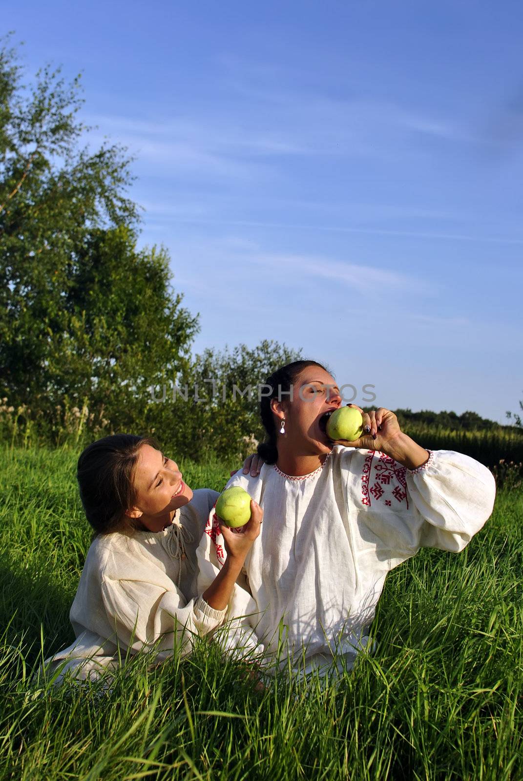 Two girls in traditional costume eating apples