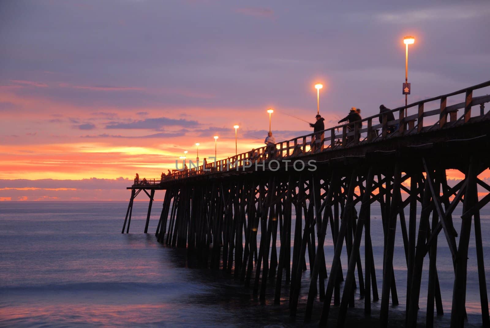 The sunrise over the pier at Kure Beach with fisherman on the pier.
