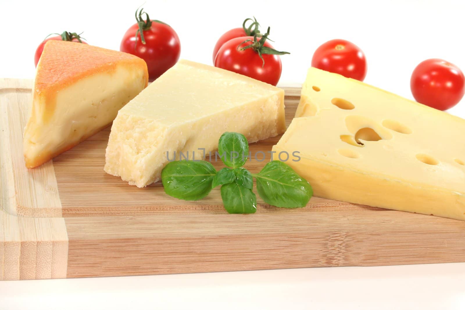 a selection of cheeses with tomato and basil on a wooden board