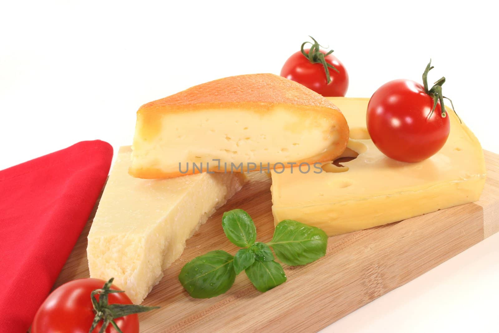 a selection of cheeses with tomato and basil on a wooden board