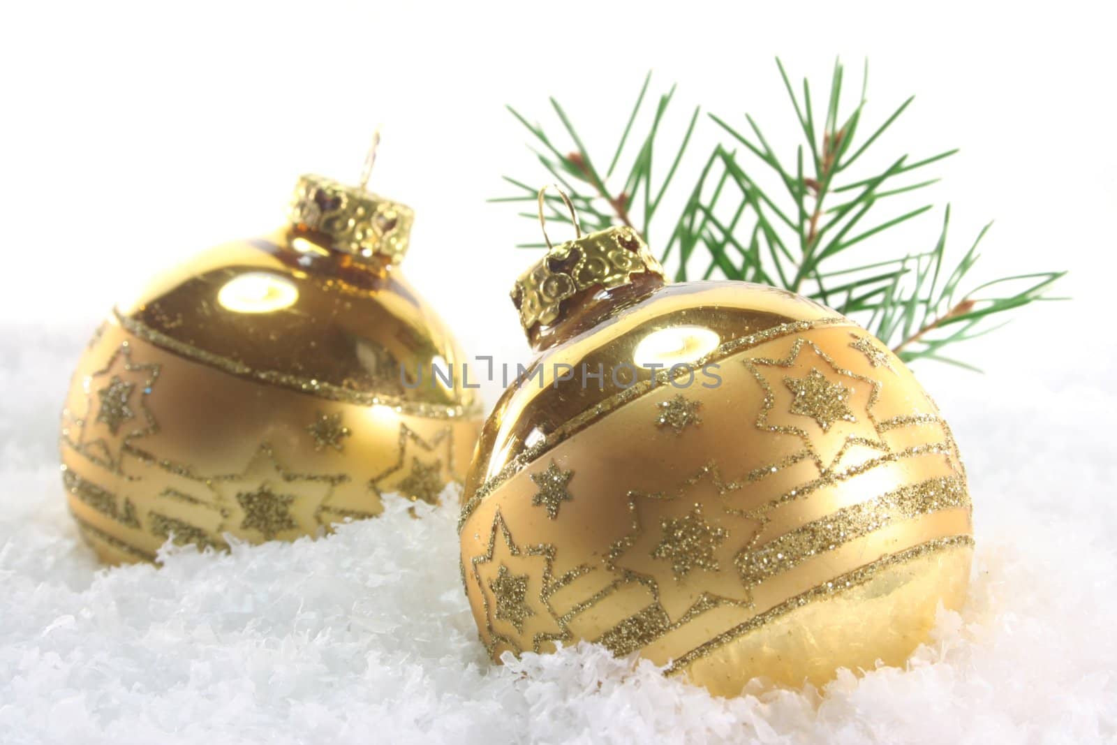 two golden Christmas balls with pine branches lying in the snow