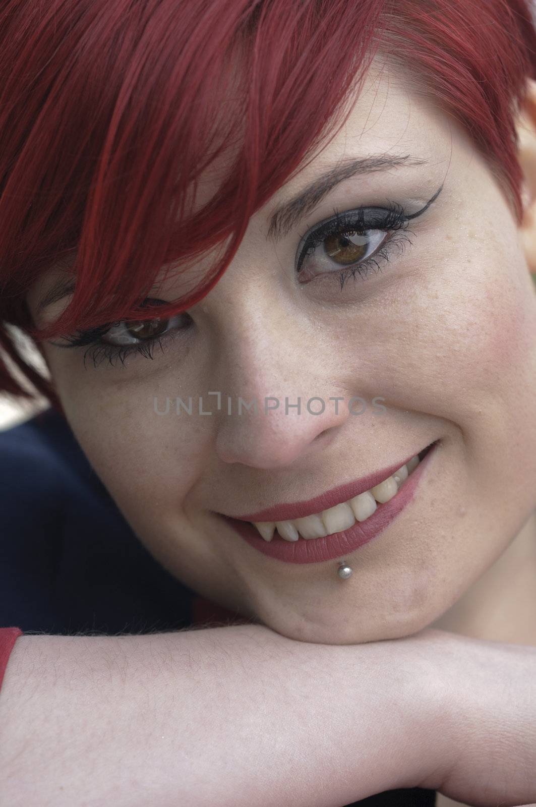Portrait of a girl with red hair, piercing on lower lip, and smiling.