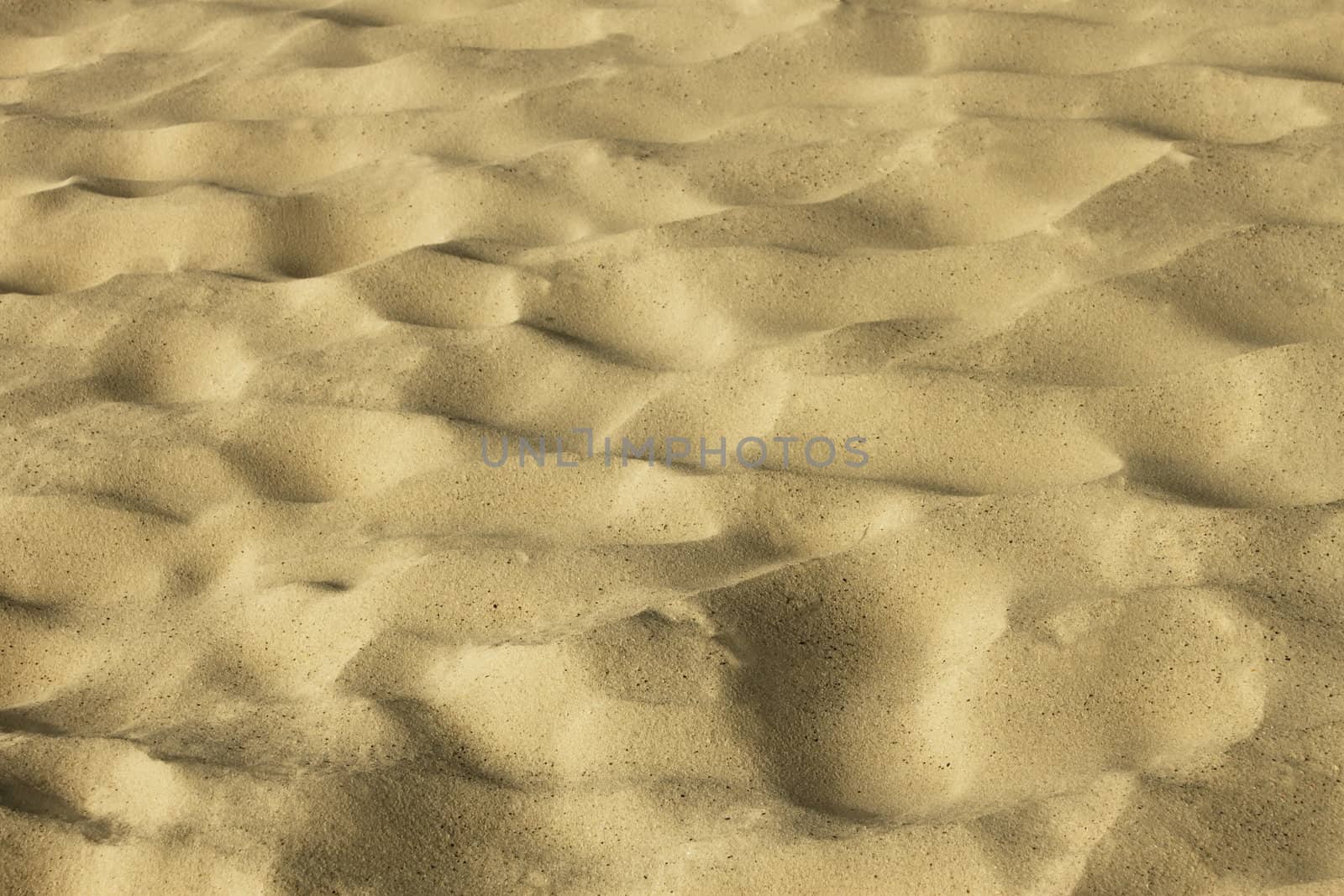 Wavy yellow sand on the beach with vague traces of people