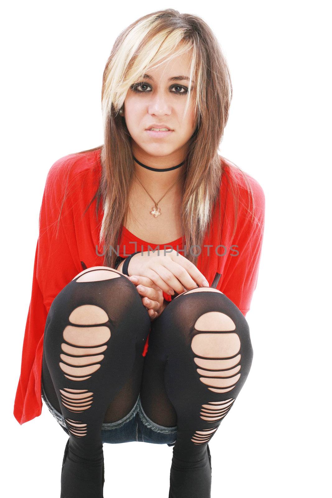 Young woman in punk attire bends over to hug her legs while looking into the camera.