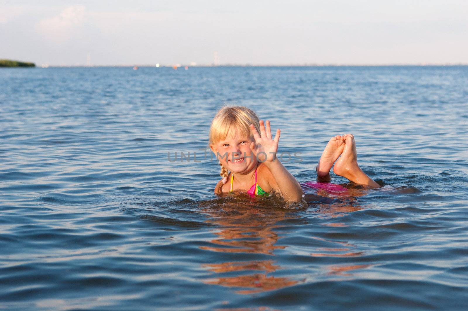 happy girl waving with hands in the water at the evening