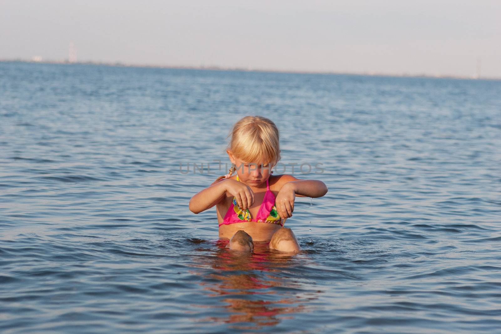 happy girl playing with sand in water at evening