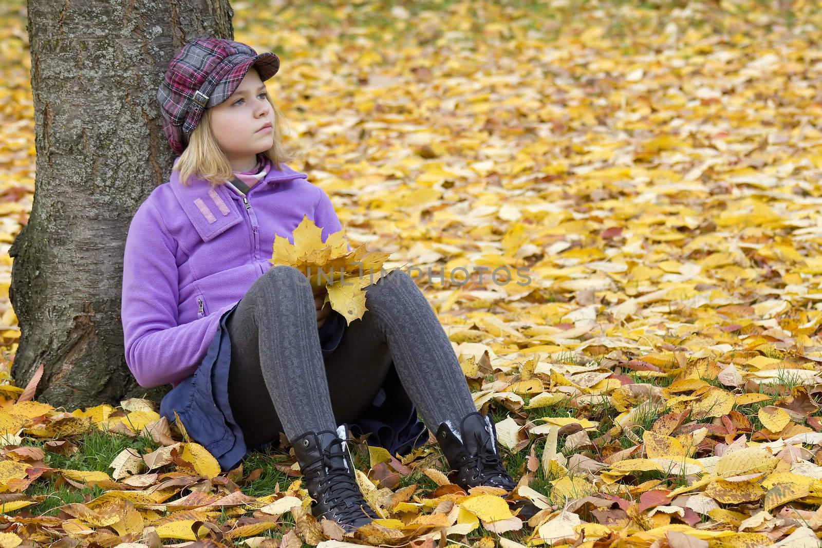 Full length portrait of a little girl sitting under tree in autumn park