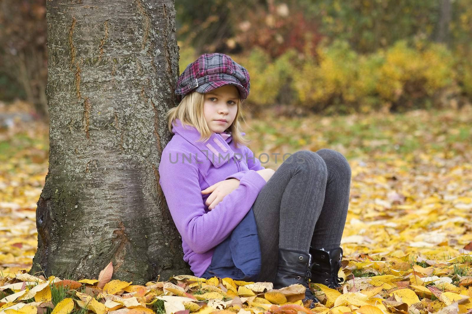 Full length portrait of a little girl sitting under tree in autumn park 