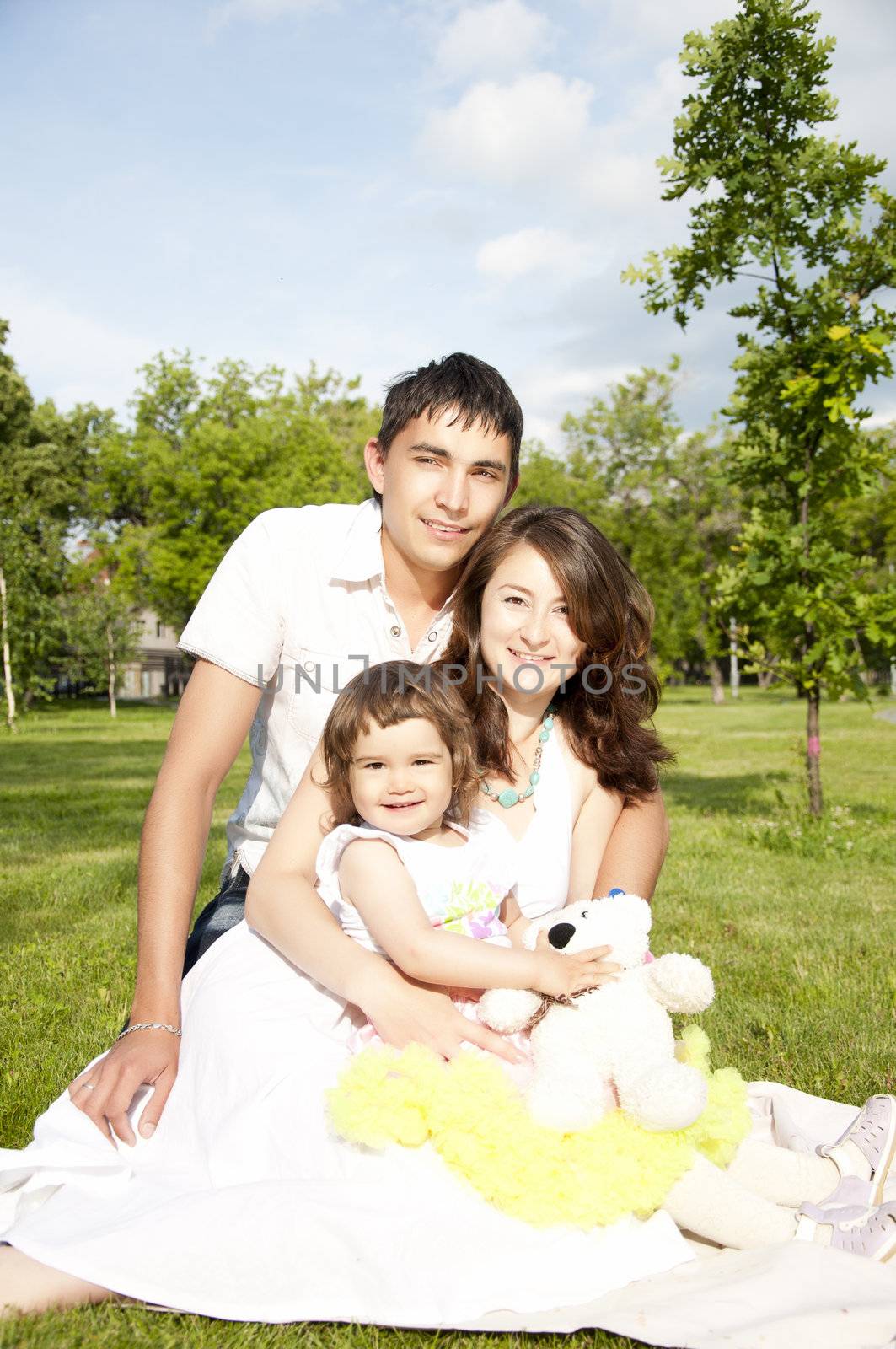 The husband, the wife and the child sit on a coverlet in park