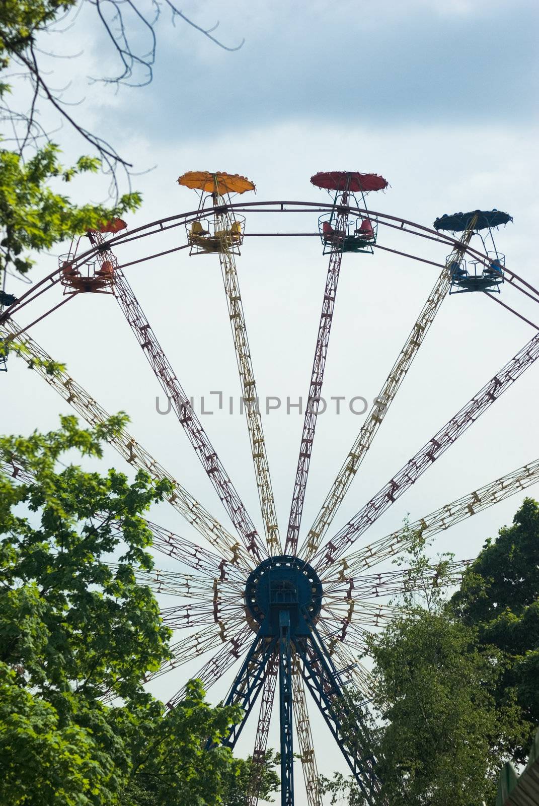 Popular attraction in park - a Ferris wheel on a background of the cloudy blue sky