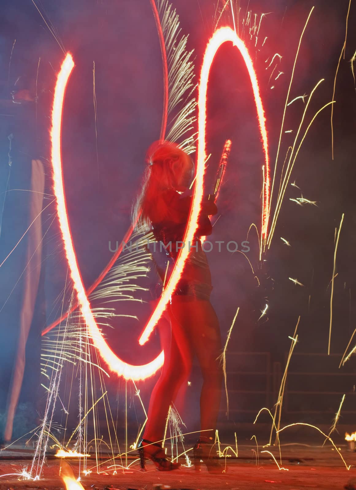 Woman performing a dangerous fire show by spinning a pole engulfed in flames.Defocused