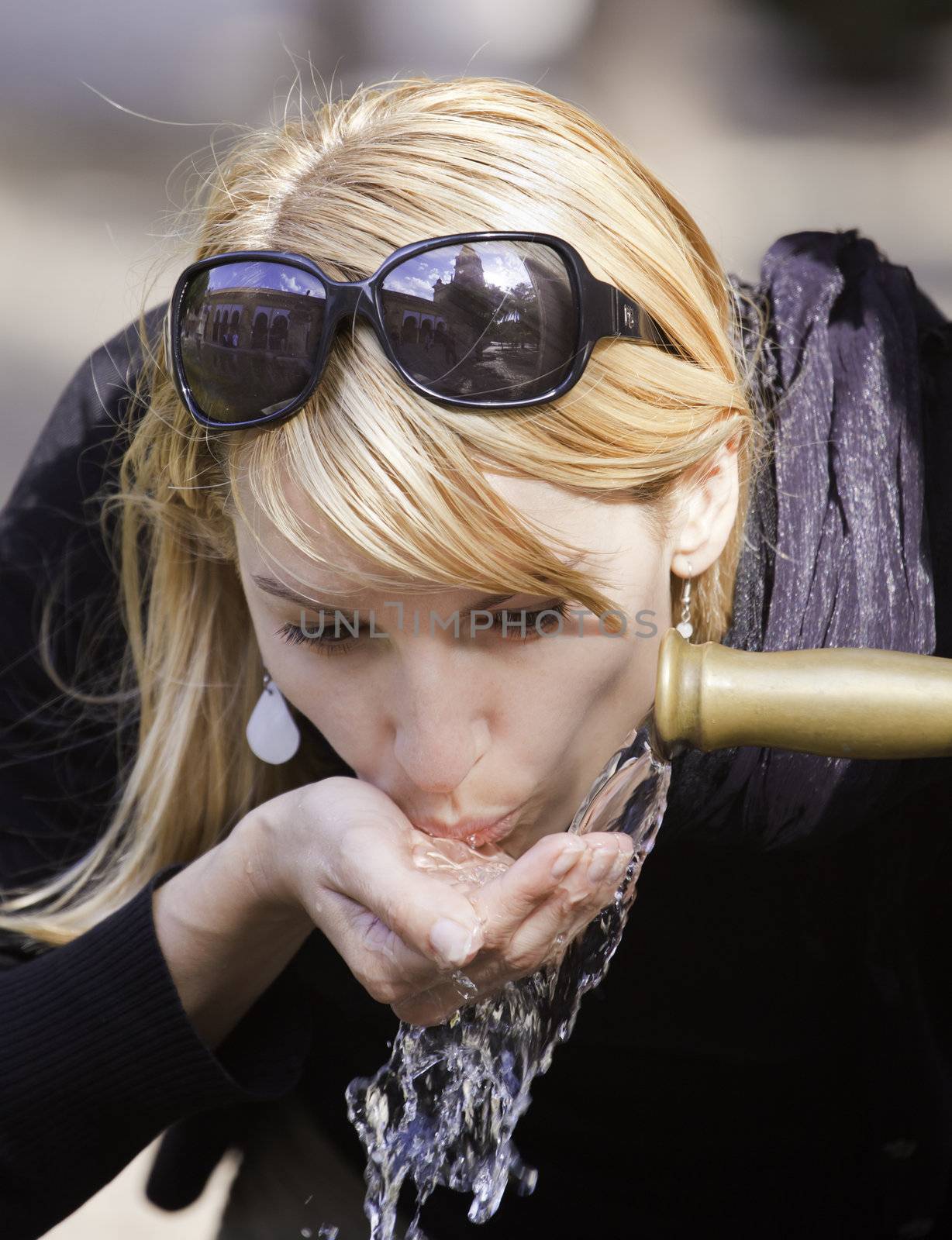 Young lady drinking tap water from the fountain in the city park on a hot summer day.