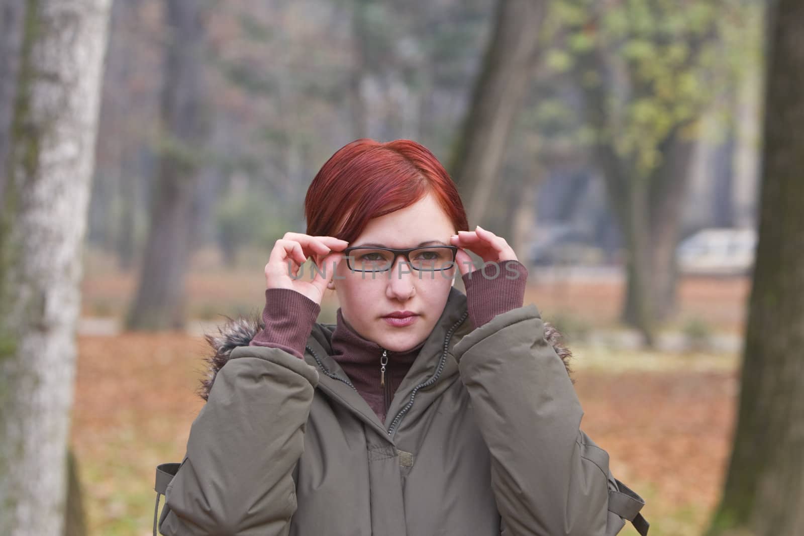 Redheaded girl putting on her glasses outdoors in an autumn park.