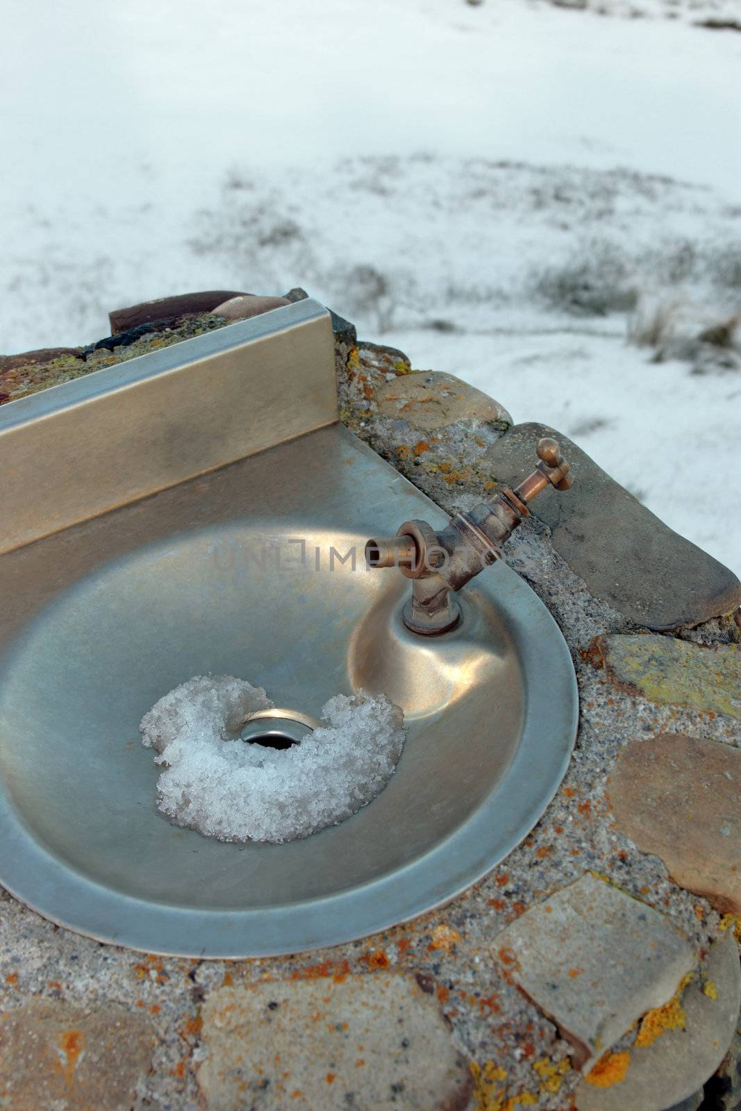 a frozen outdoor water tap against a winters snow background