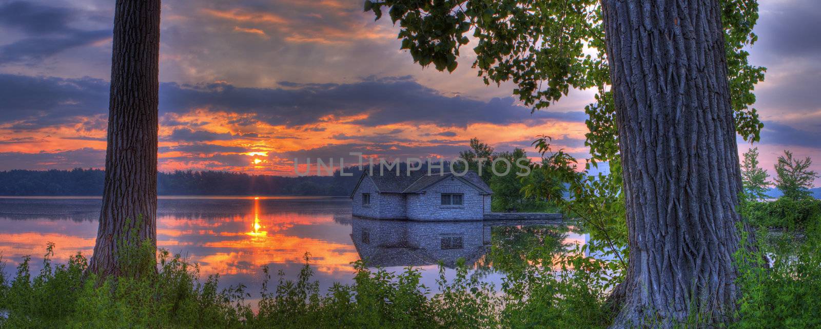 Panorama of a sunrise and pump house utility on a lake.