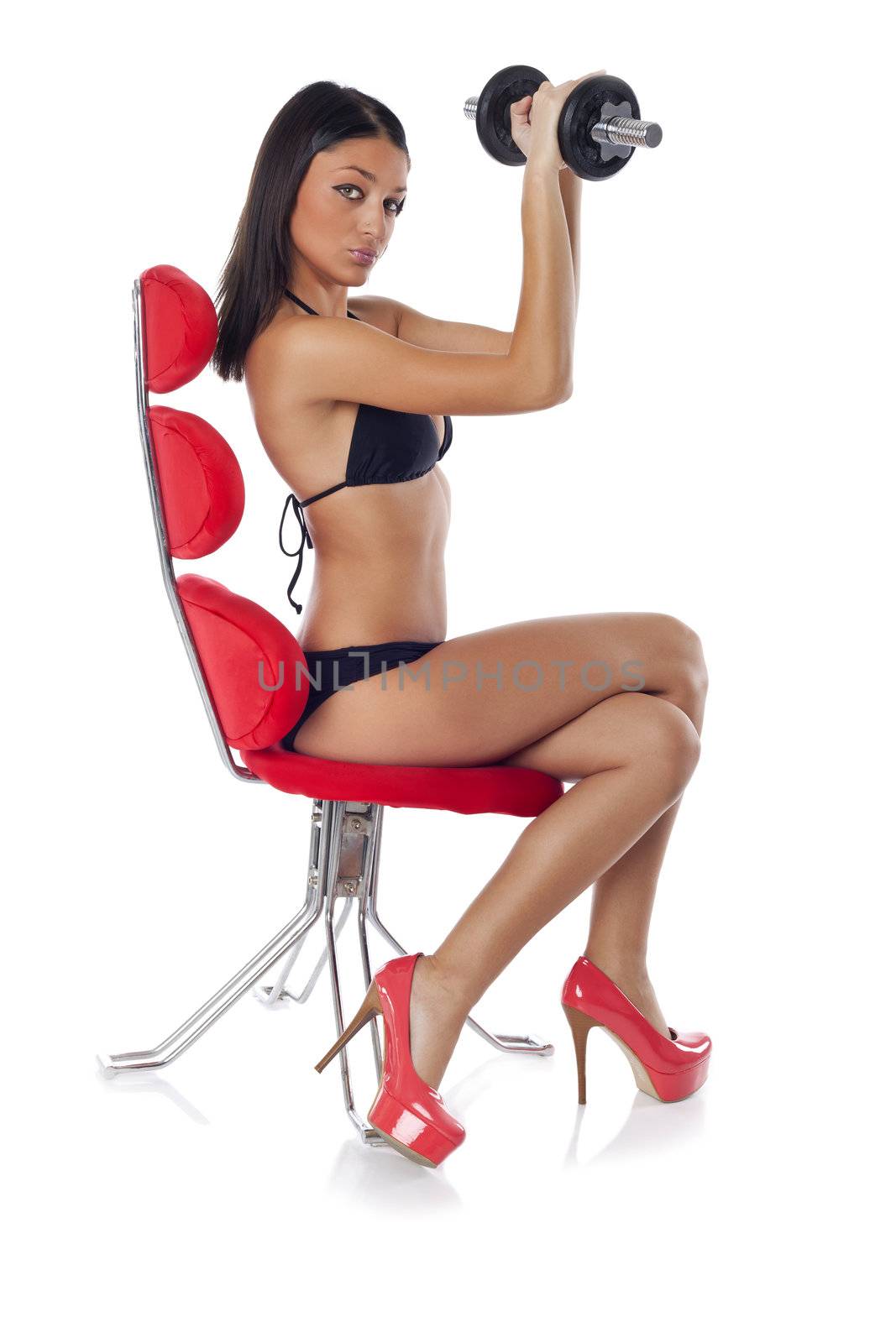 Beautiful woman sitting on red chair and training with dumbbells 