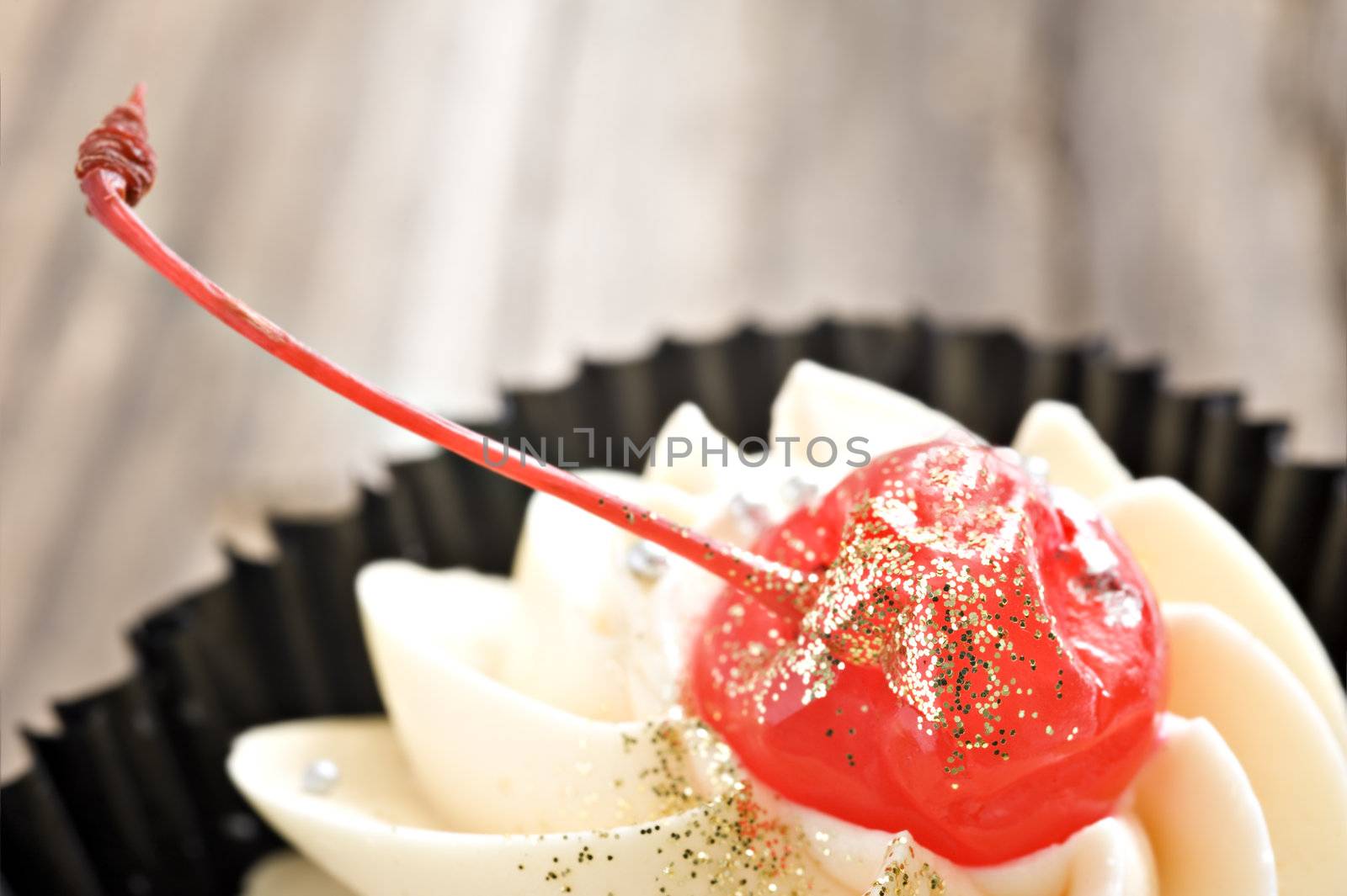 Very close up image of a cup cake with a red cherry - very shallow depth of field