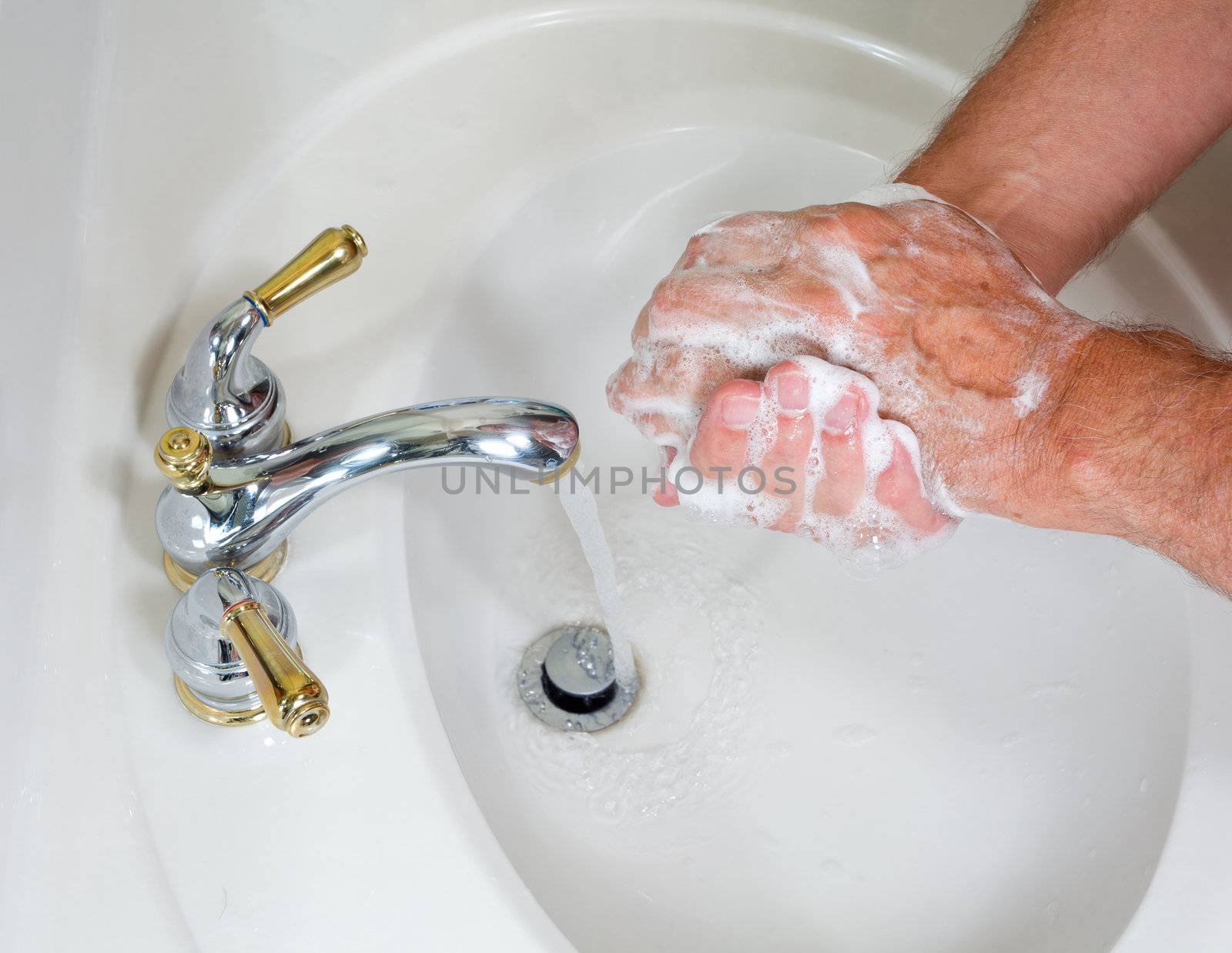 Senior man washing hands in modern sink with soap and lathering suds