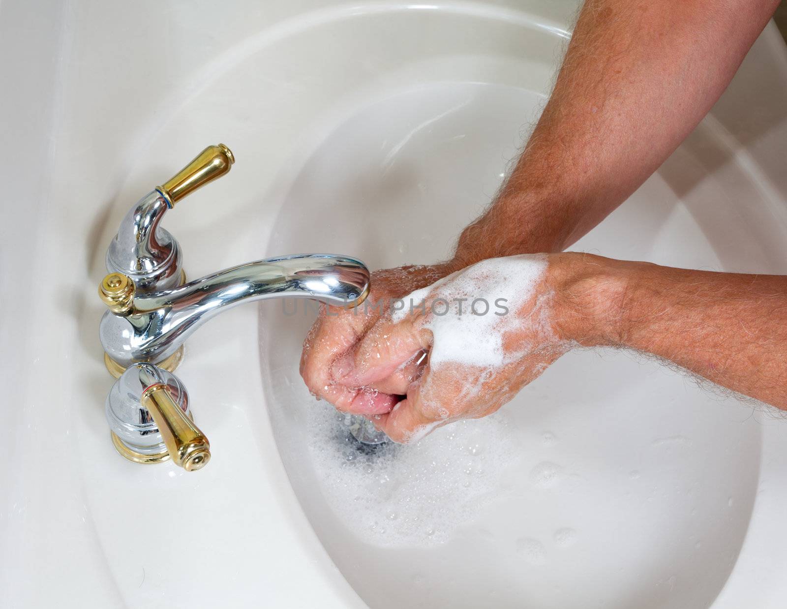 Senior man washing hands in modern sink with soap and lathering suds