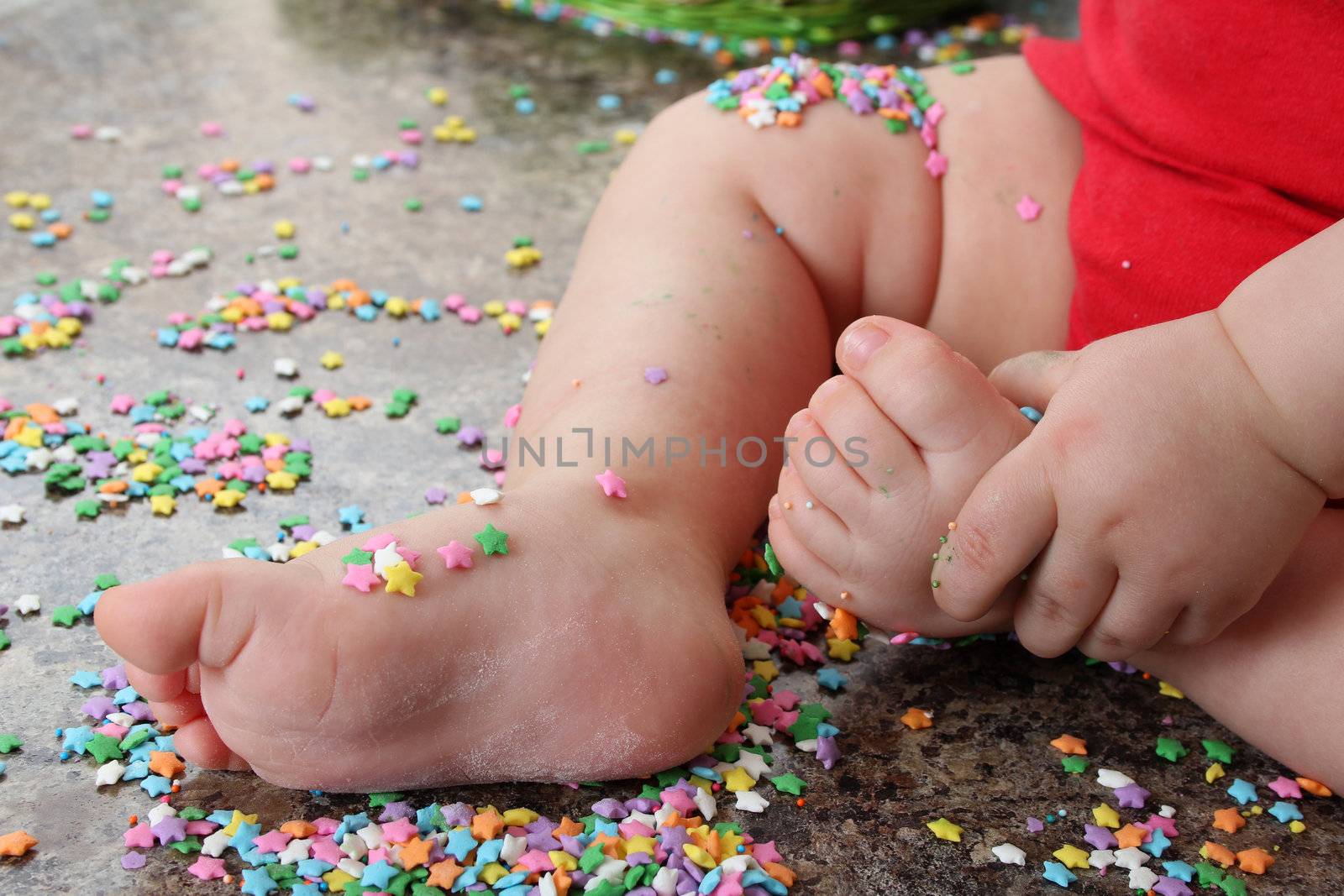 Baby feet and hand on kitchen countertop surrounded with cake decorations