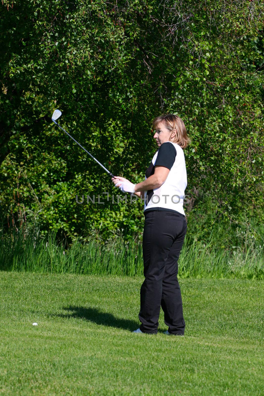 Adult female golfer playing an iron shot from the fairway