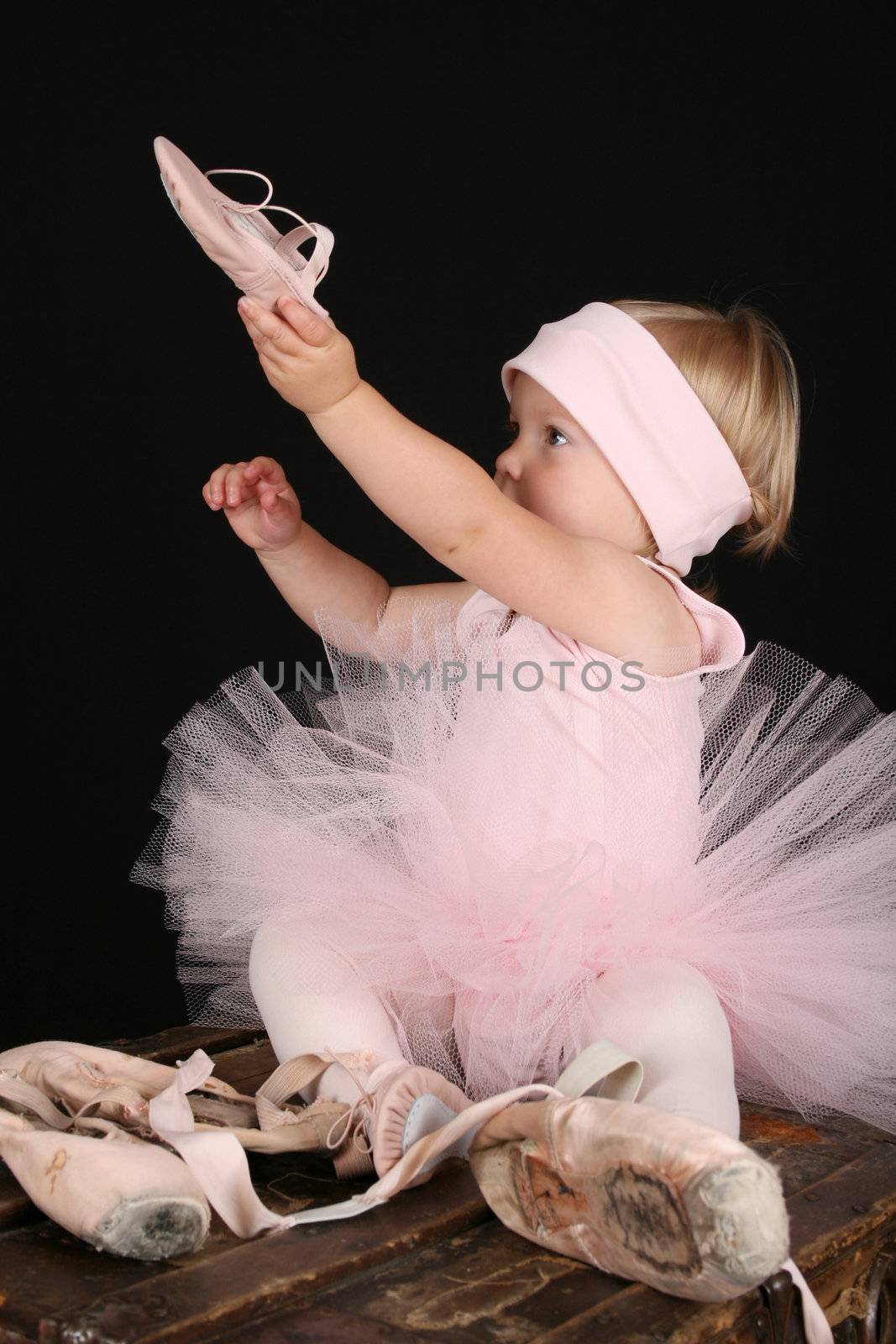 Blond toddler wearing a tutu holding Ballet shoes 