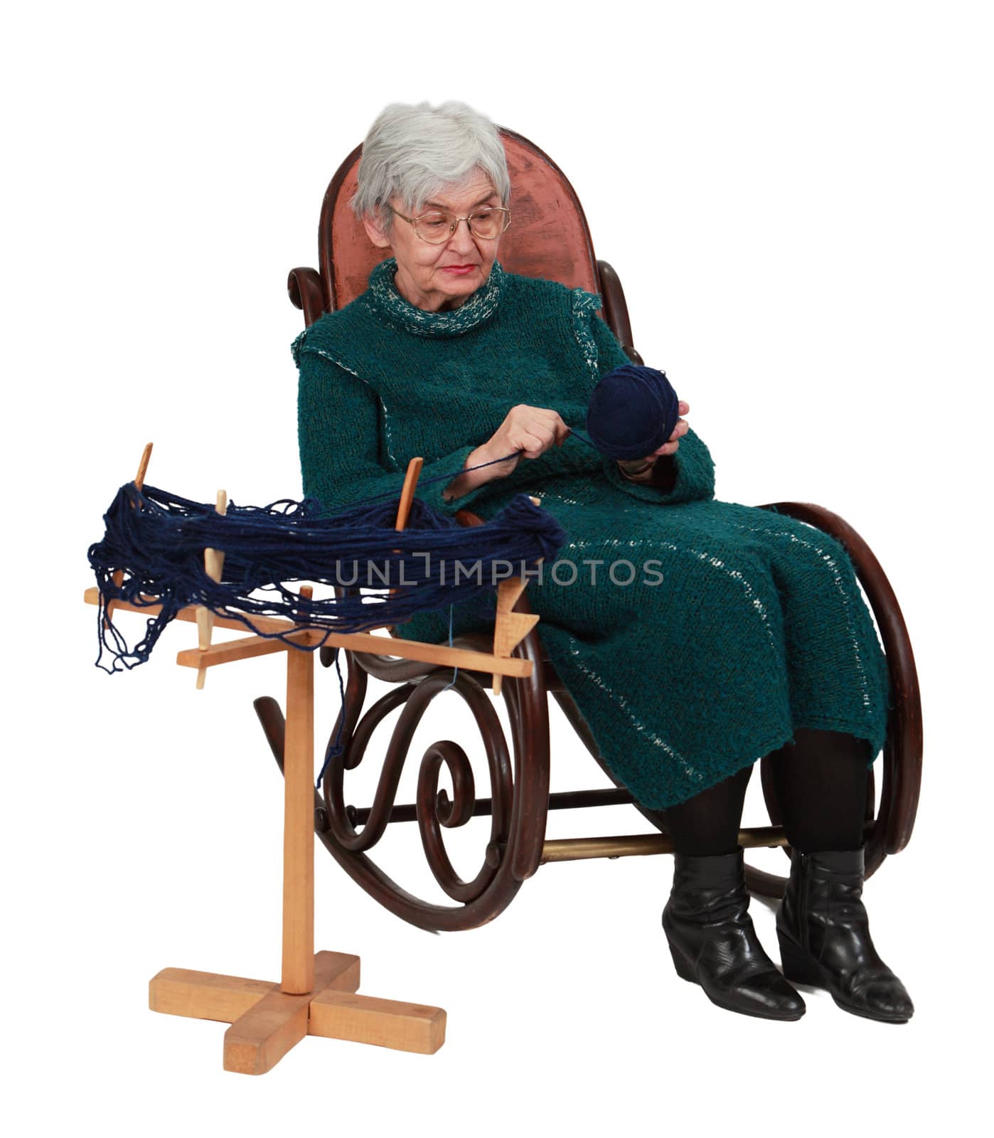 Old woman sitting on a rocker and making a ball of thread using a reel, isolated against a white background.