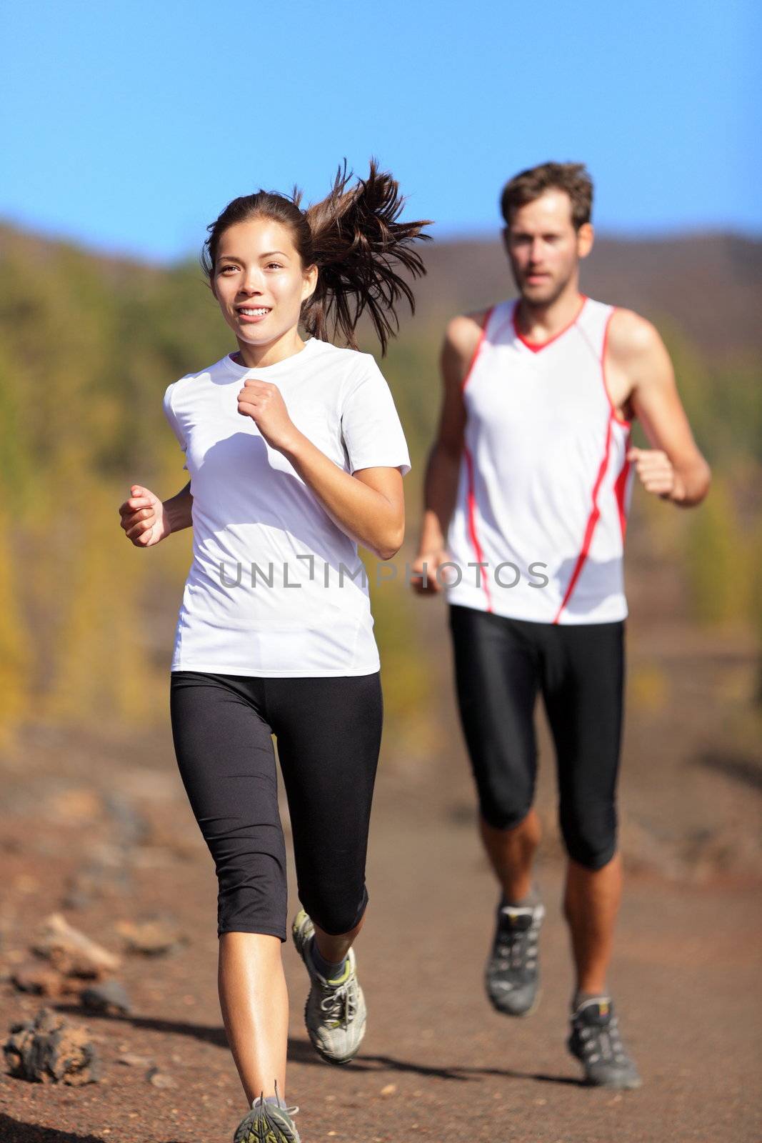 Young couple running together outdoors in beautiful volcanic landscape. Woman trail runner training for marathon run with male model jogging in background.
