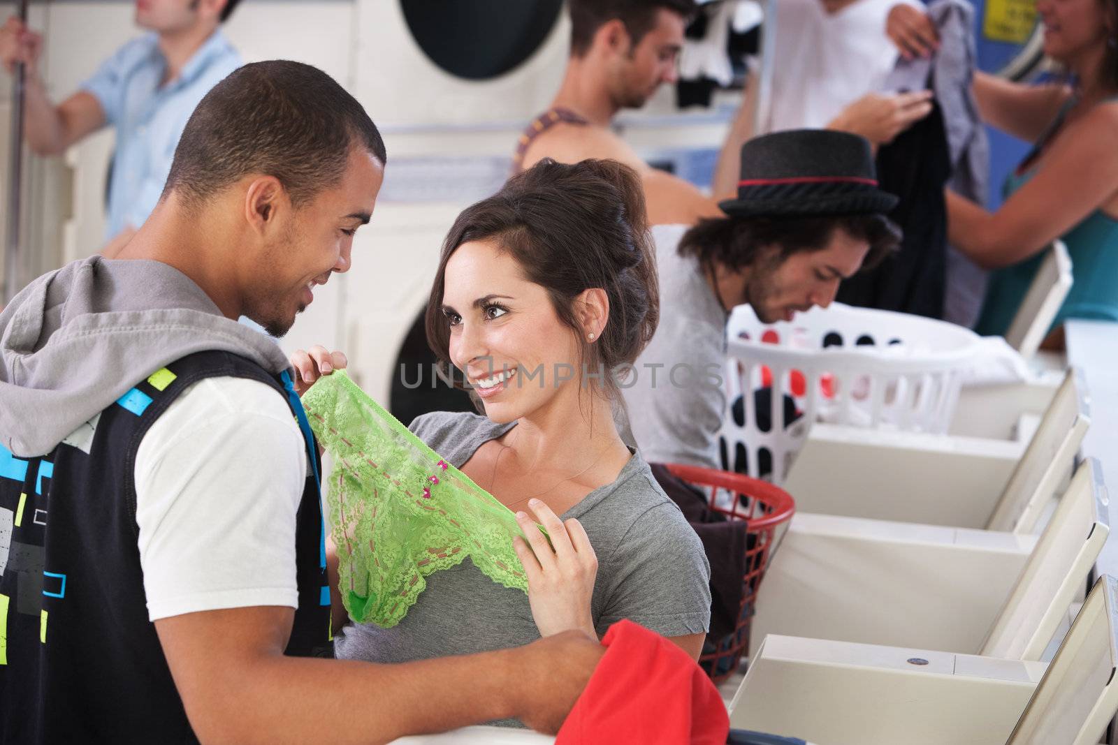 Young lady holding underwear in front of man in laundromat