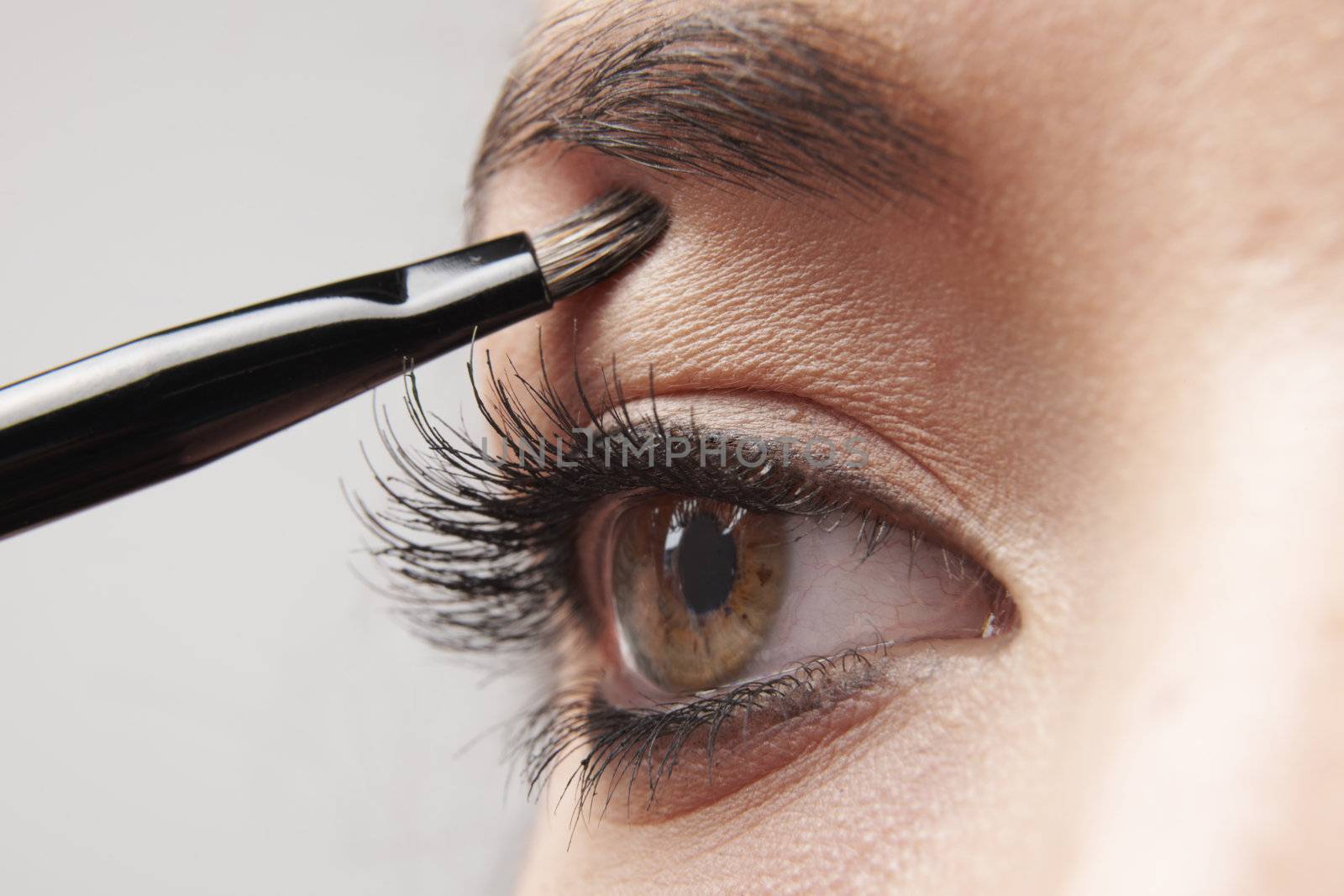 woman applying eye make-up with brush on white background