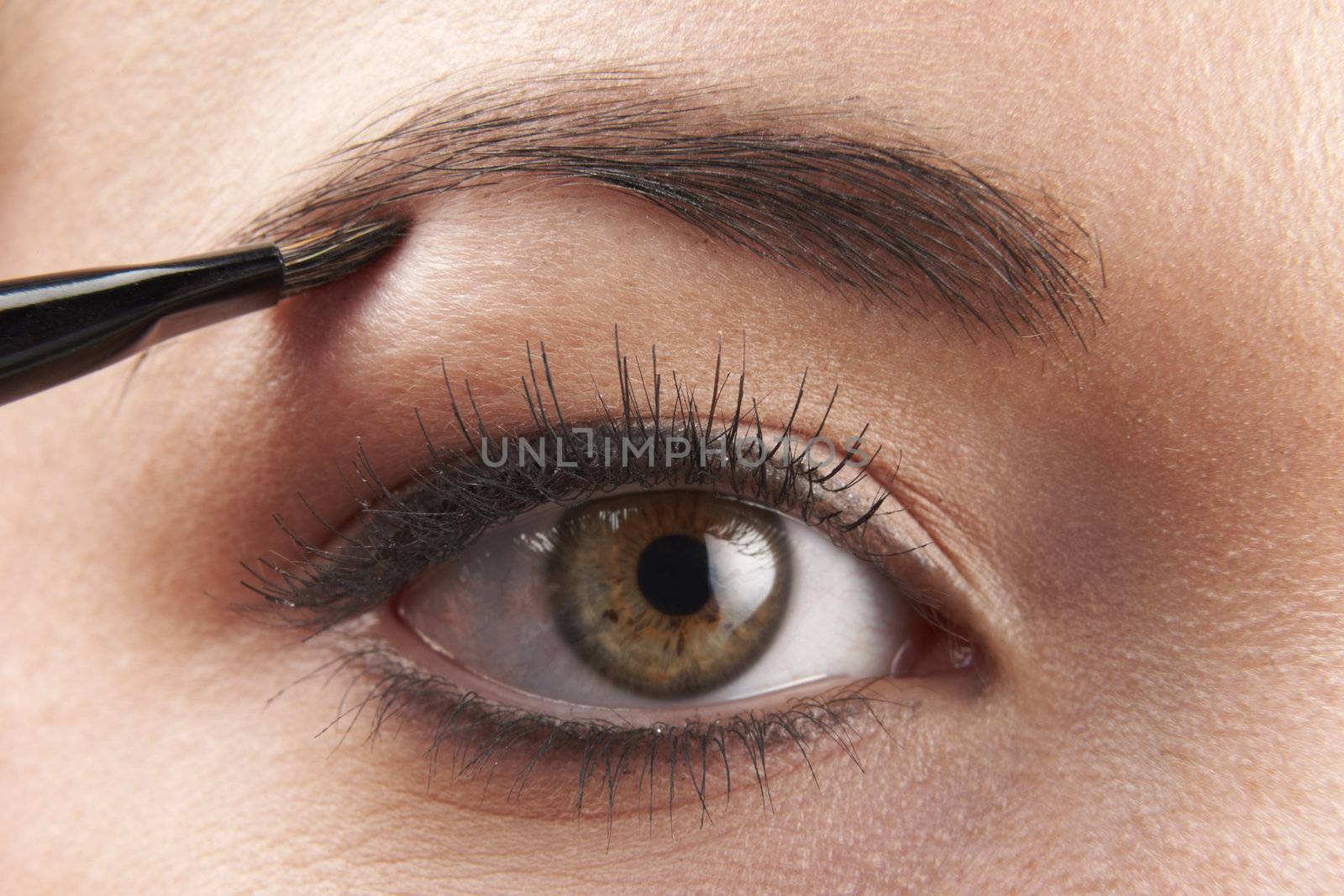 woman applying eye make-up with brush on white background