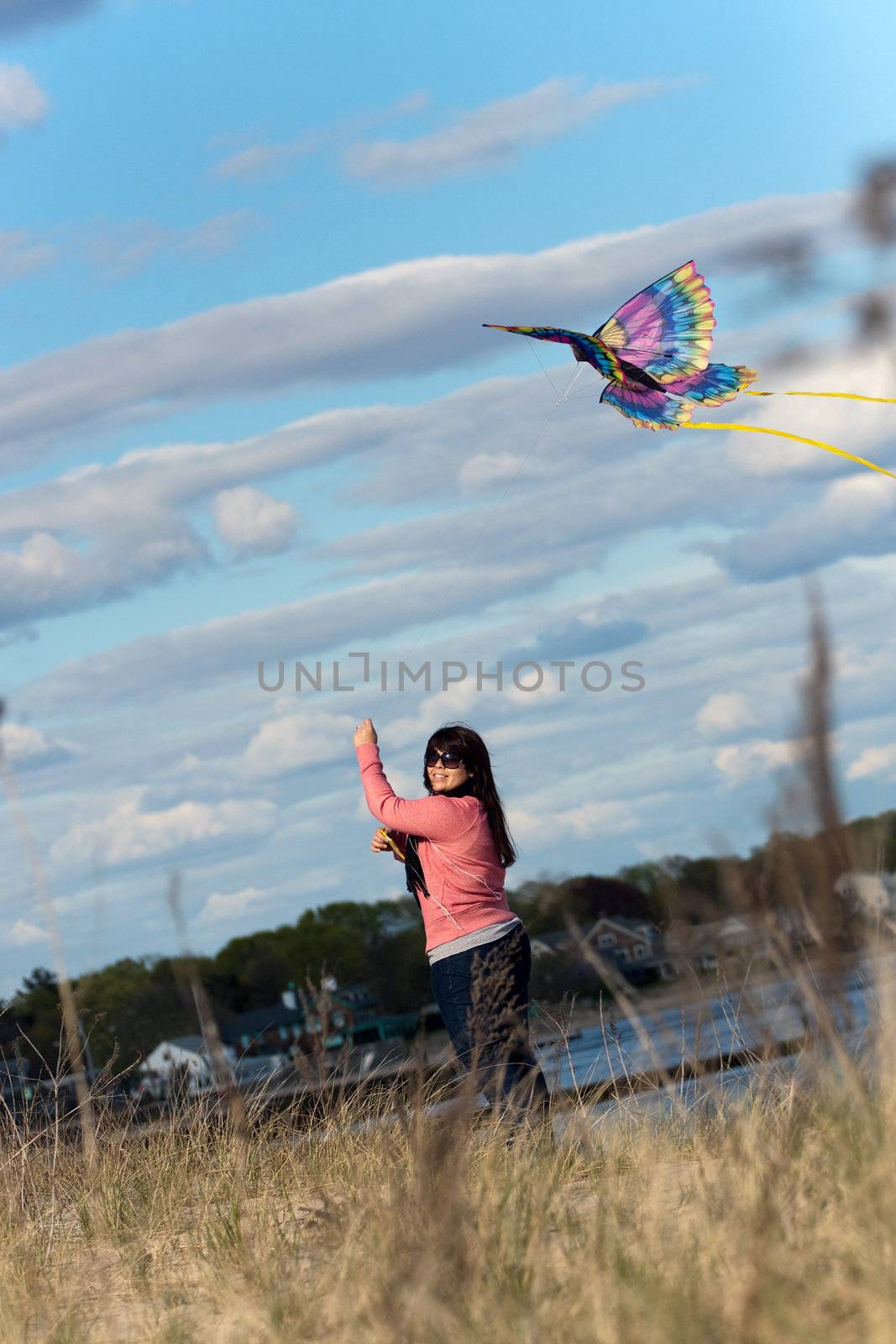 A young brunette woman flies a kite at the beach on a nice day.