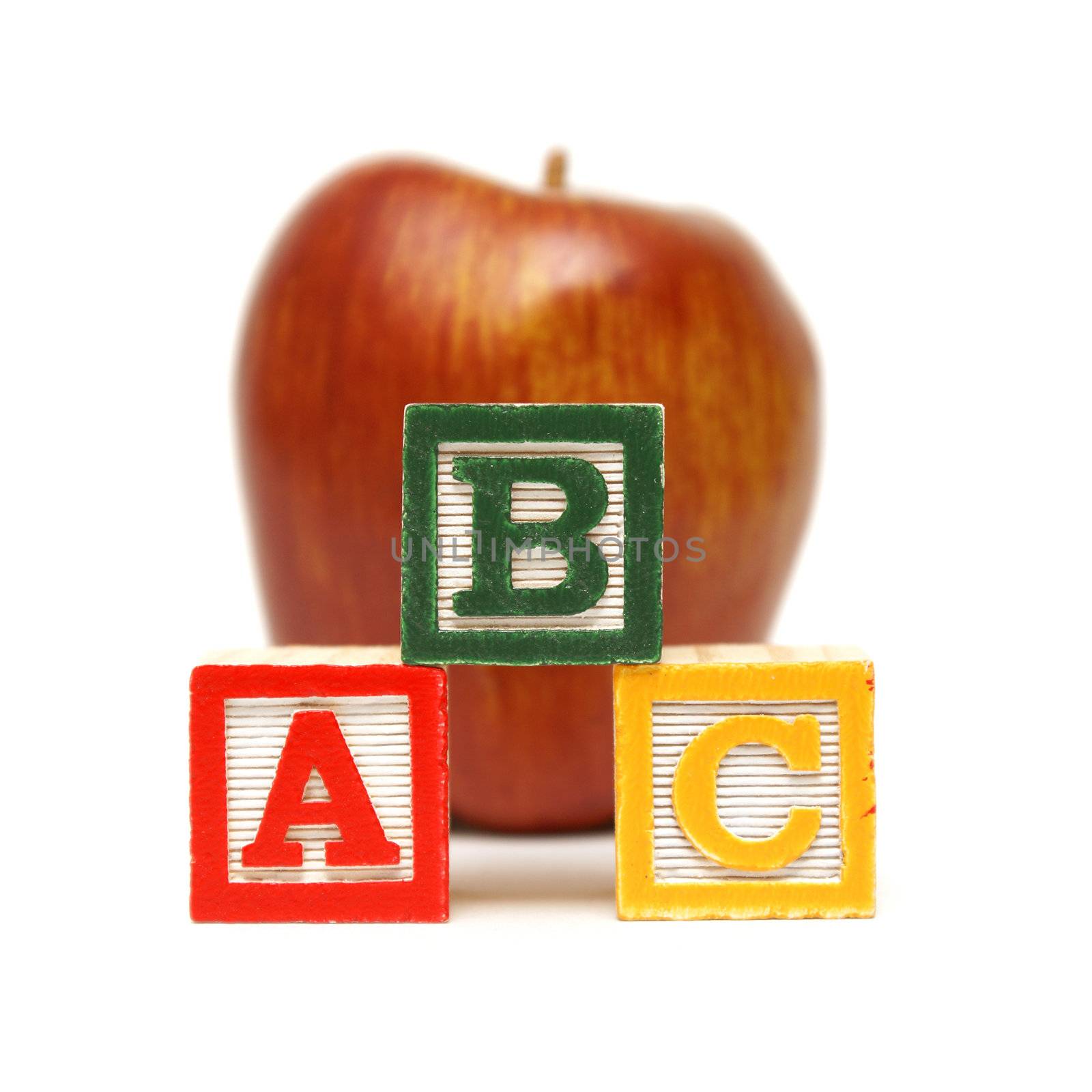 Three learning blocks are stacked up in front of a nice red apple for the young mind at work.