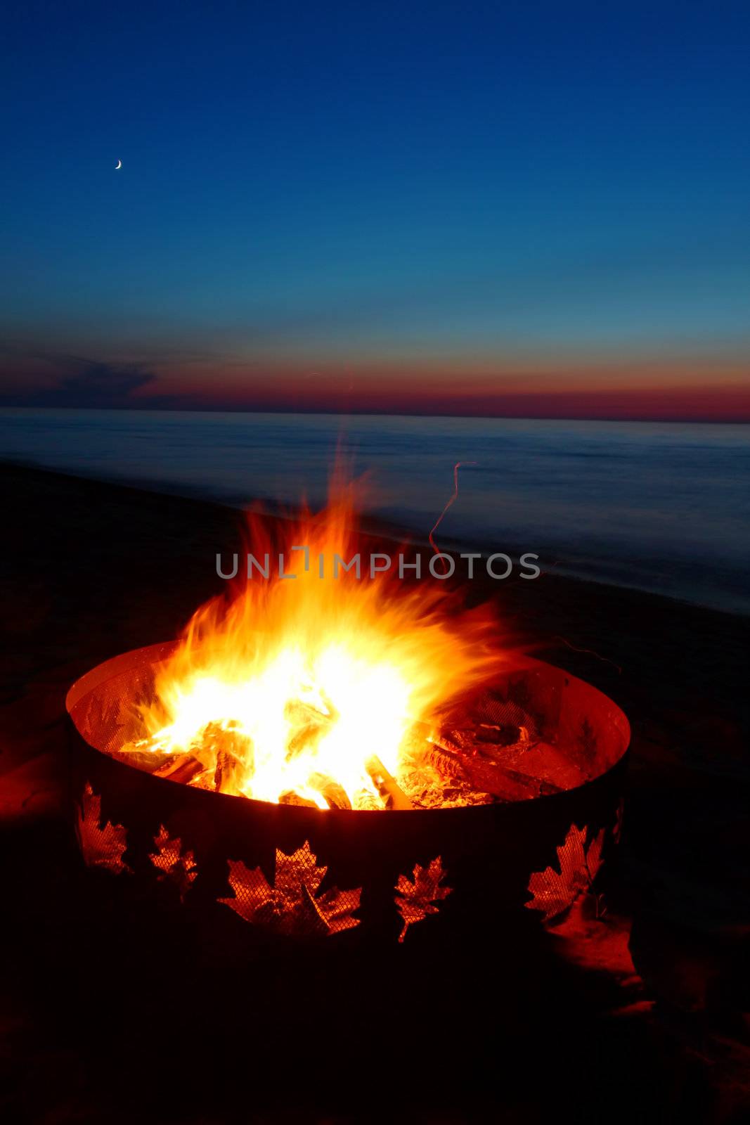 Campfire burns brightly at sunset along the beautiful beach of Lake Superior in northern Michigan.