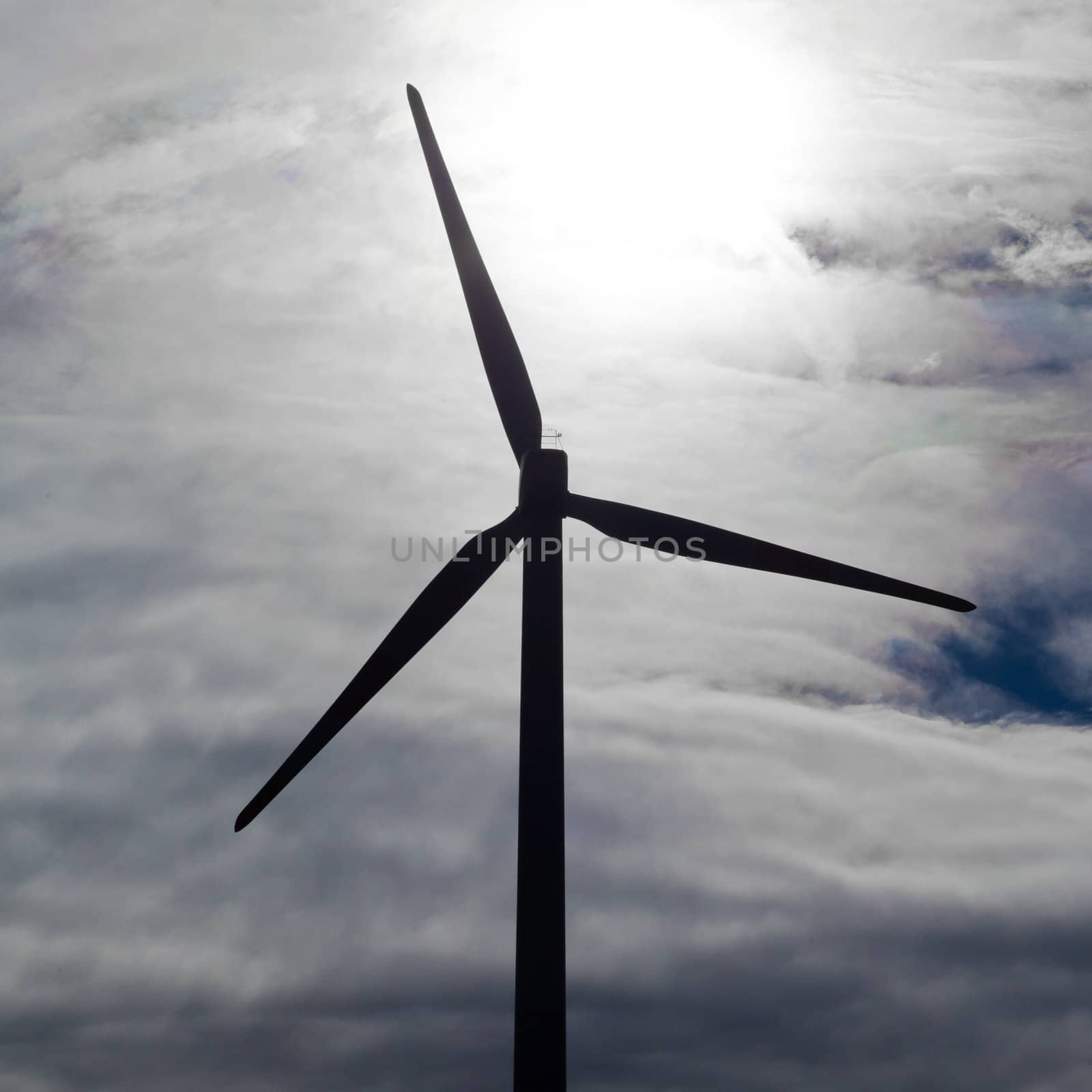Silhouette of green energy producing large wind turbine against cloudy and windy sky.