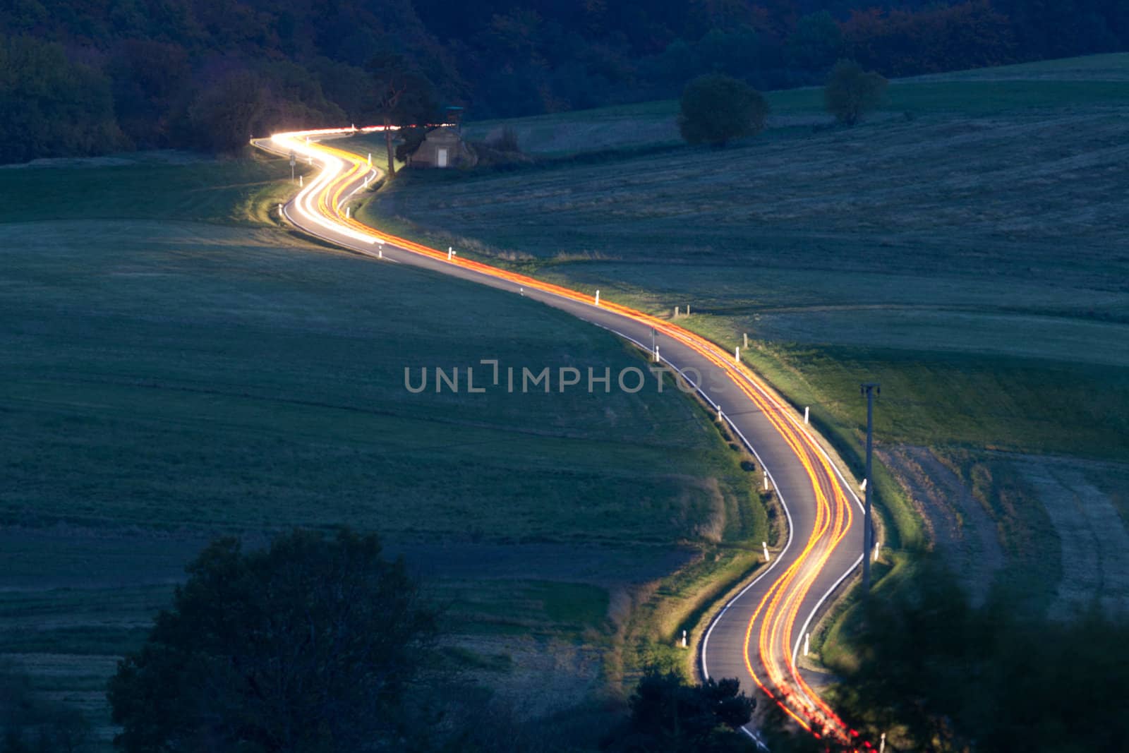 Light trails of moving vehicles on rural country road at night fall.