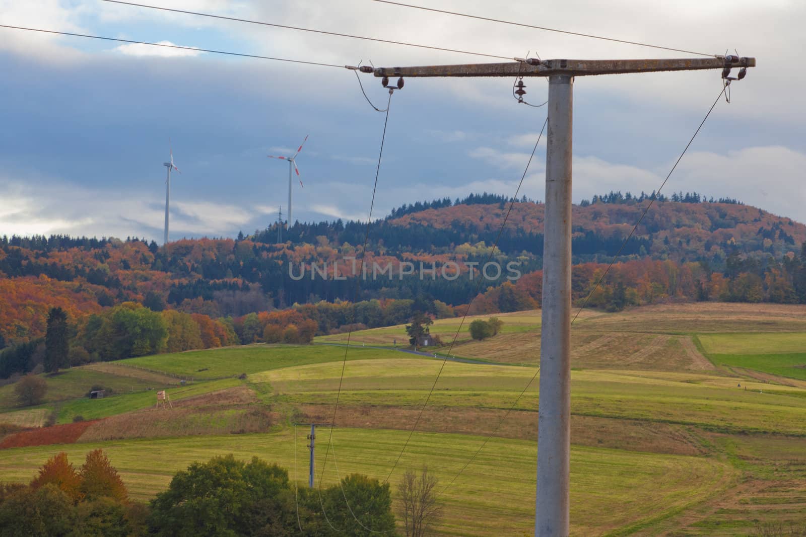Large wind turbines on the horizon of Eifel, rural Germany, Europe, with high-voltage transmission line in foreground.