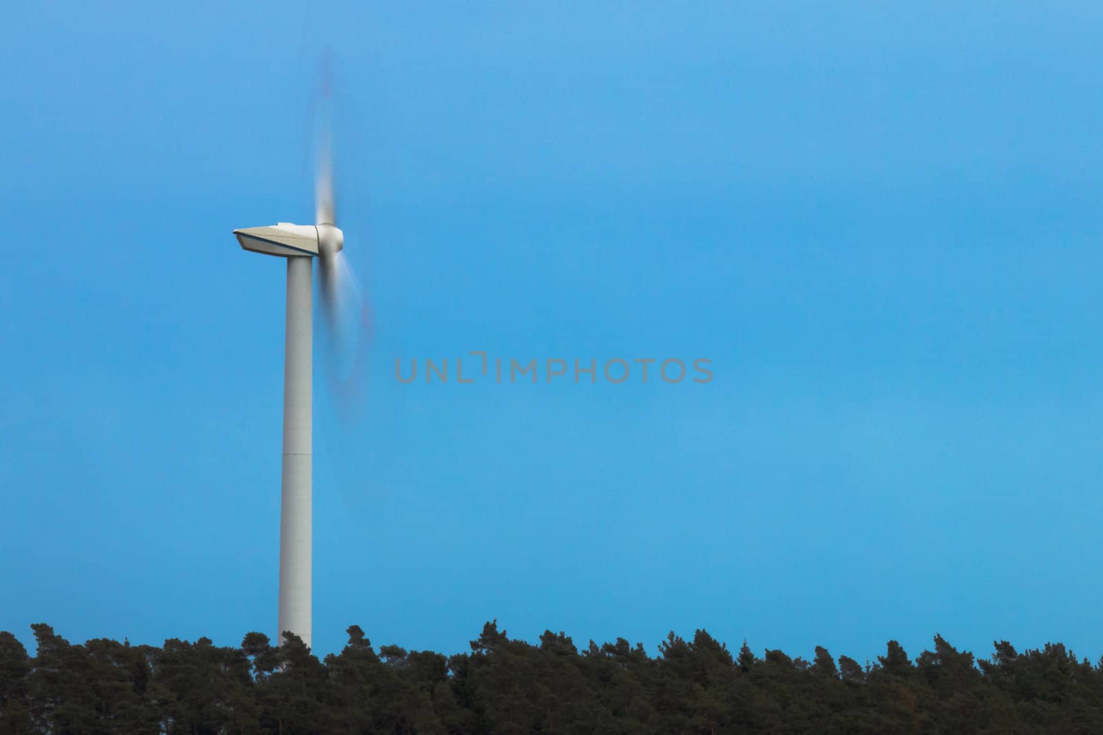 Green energy from wind: large wind turbine rotates fast (motion blur) high above forest tree tops.