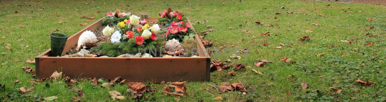 Tomb covered with colored flowers with autumn colored red leaves in a cemetery