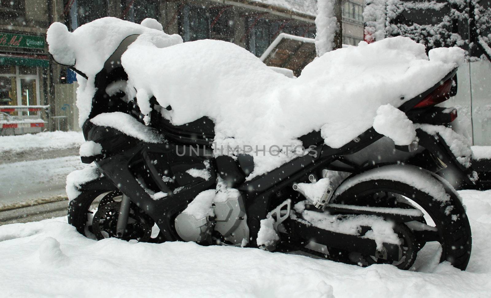 Big black motorbike covered with snow by winter weather in a street of Geneva, Switzerland