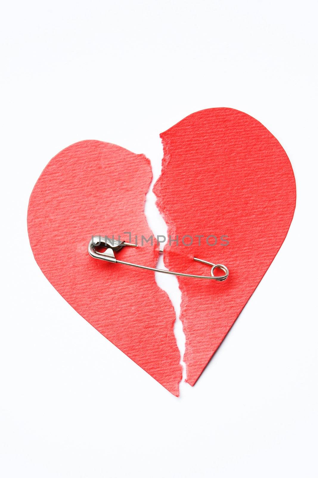 Red paper heart torn in half secured with safety pin on white background